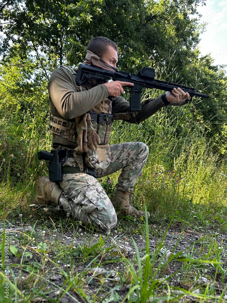 Fototapeta premium A soldier aiming a rifle. A soldier with a rifle in his hand standing in the forest. Dressed in camouflage.