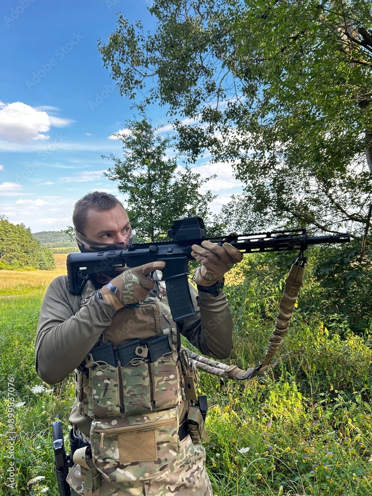 Fototapeta premium A soldier aiming a rifle. A soldier with a rifle in his hand standing in the forest. Dressed in camouflage.