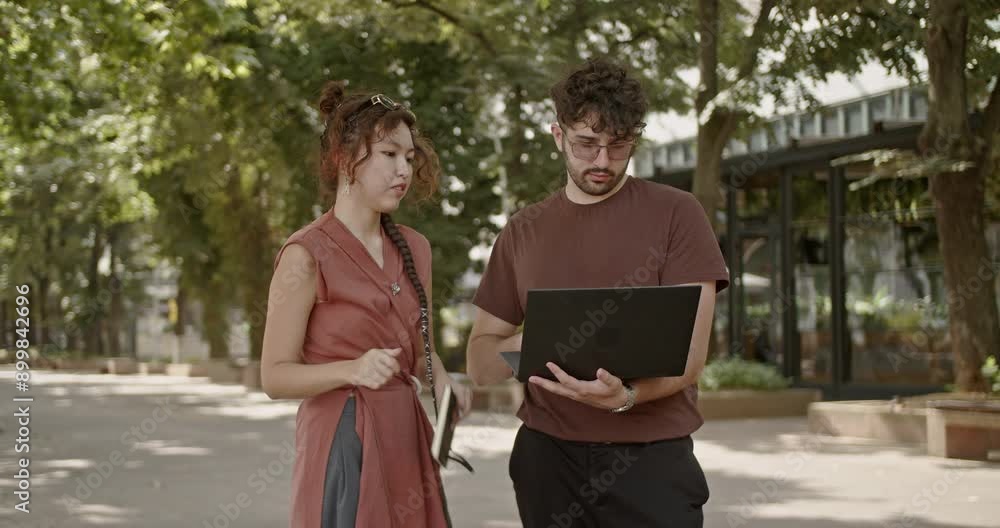 In a natural, outdoor park setting, two young adults work together on a laptop, demonstrating collaborative teamwork amidst the greenery and fresh air. In a natural, outdoor park setting, two young adults work together on a laptop, demonstrating collaborative teamwork amidst the greenery and fresh air.