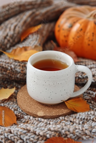 warm cup of tea resting on a cork coaster, surrounded by a knitted brown blanket and scattered autumn leaves