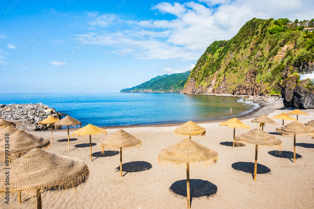 Sun umbrellas on beach in Povoacao town and green hills in background, Sao Miguel island, Azores, Portugal