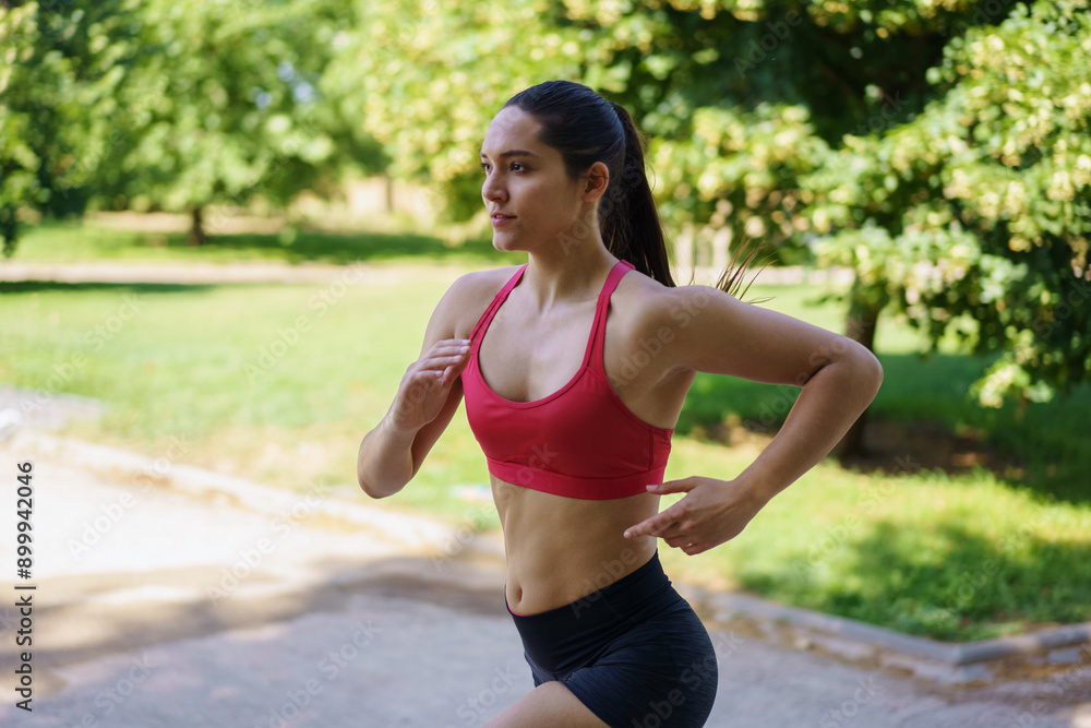 A woman is jogging in a park on a sunny day, dressed in sportswear, showcasing her dedication to an active lifestyle A woman is jogging in a park on a sunny day, dressed in sportswear, showcasing her dedication to an active lifestyle