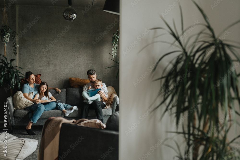 Focused parents homeschooling son and daughter sitting on sofa at home Focused parents homeschooling son and daughter sitting on sofa at home