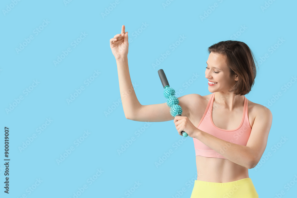 Sporty young woman massaging her arm with roller on blue background Sporty young woman massaging her arm with roller on blue background