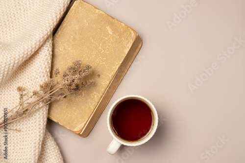 Vintage book, scarf and cup tea on beige background. Leisure concept, reading a book. Flat lay, top view