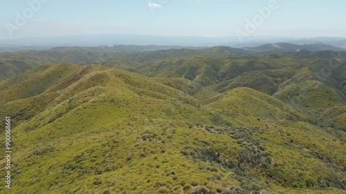 Drone flying over green hills with yellow flowers with a hazy sky in California