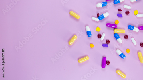 Multi-colored pills and capsules used in medical treatment are scattered on a pink background. Colorful pills and capsules. Healthcare and medical concept. Space for text.