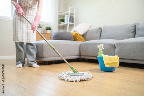 Housekeeper mopping the laminate wooden floor and cleaning dust during chores daily routine.