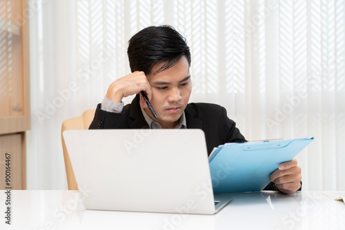 Professional young manager contemplating a project on his worktable with a laptop in an office setting, capturing themes of business strategy, executive focus, and productive thinking.