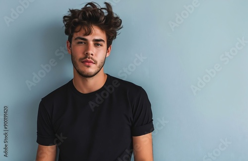 A young man in a black shirt leaning against a blue wall