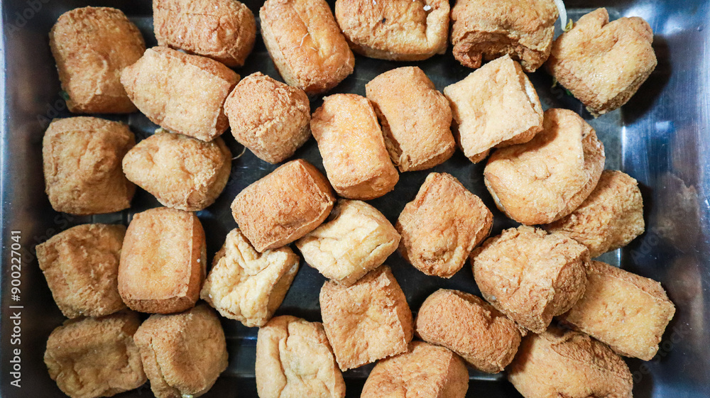 A close-up view of a tray filled with fried tofu cubes, a popular Asian snack or appetizer known for its crispy texture and savory flavor. Fried Tofu Background. A close-up view of a tray filled with fried tofu cubes, a popular Asian snack or appetizer known for its crispy texture and savory flavor. Fried Tofu Background.