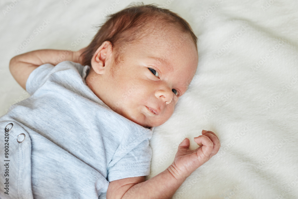 Newborn infant lying on the bed on white sheet little kid dressed in bodysuit looking away with curious eyes space available for advertisement or promotional text Newborn infant lying on the bed on white sheet little kid dressed in bodysuit looking away with curious eyes space available for advertisement or promotional text