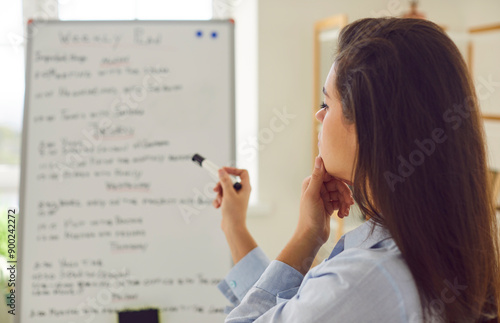 Focused woman, immersed in creating a event plan or schedule for the week on a whiteboard. The image captures the essence of strategic work, organization timeline, and meticulous planning agenda.