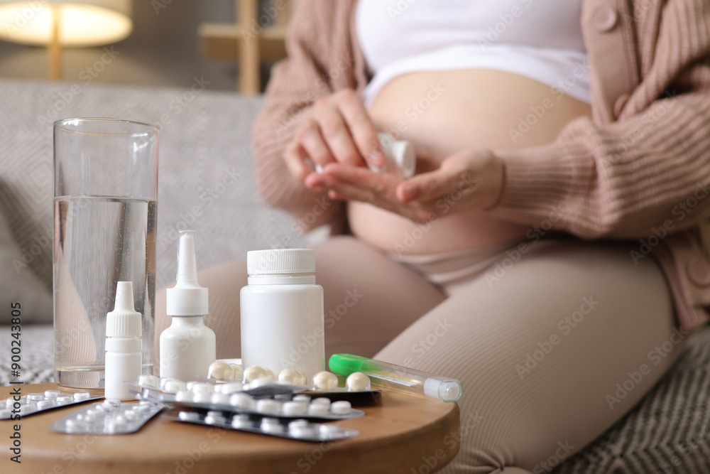 Unrecognizable anonymous pregnant woman holding plastic jar with pills taking vitamins and minerals treating sickness during pregnancy sitting on sofa at home Unrecognizable anonymous pregnant woman holding plastic jar with pills taking vitamins and minerals treating sickness during pregnancy sitting on sofa at home