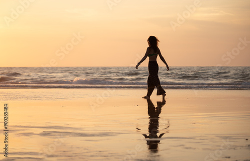 young girl enjoying a walk along the beach shore at sunset
