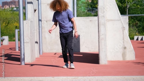 Latin young man with curly long hair doing acrobatic jumps in a parkour park