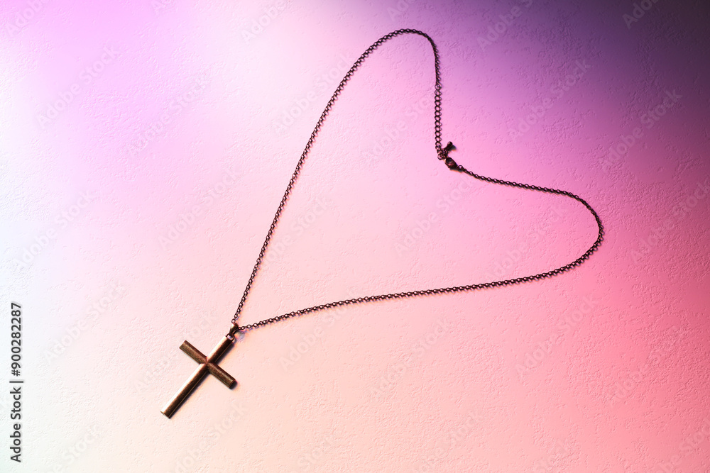 Cross with chain on textured table in color lights, top view. Religion of Christianity Cross with chain on textured table in color lights, top view. Religion of Christianity