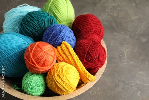 Different yarns and knitting sample in bowl on grey textured table, closeup photo