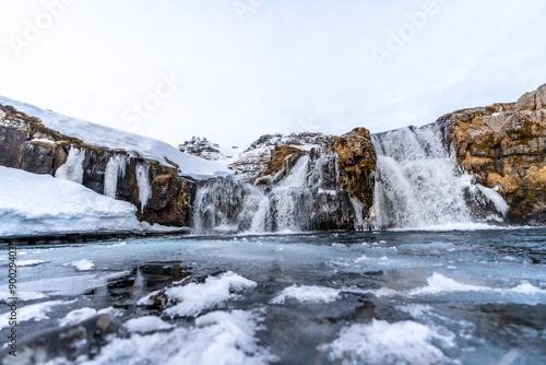 Frozen waterfall next to famous Kirkjufell mountain in Iceland winter