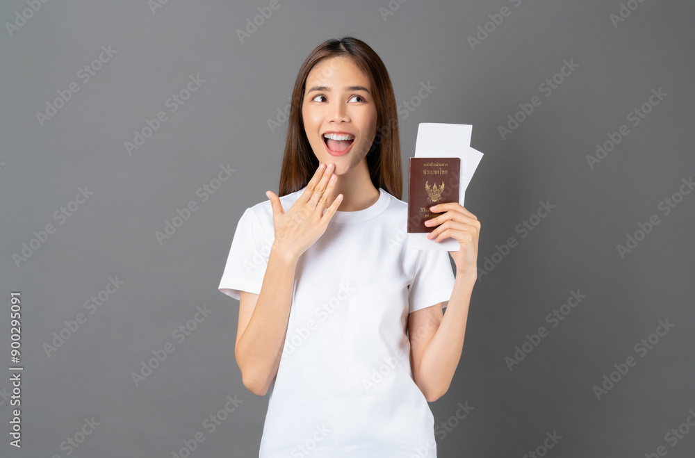 Happy cheerful young woman standing and holding passport with ticket on grey background. Travel concept. Happy cheerful young woman standing and holding passport with ticket on grey background. Travel concept.