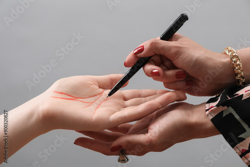 Фотография Fortune teller reading lines on woman's palm against light grey background, closeup