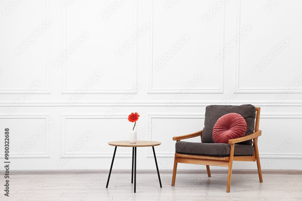 Fototapeta premium Comfortable armchair with pillow and coffee table near white wall, space for text. Interior design