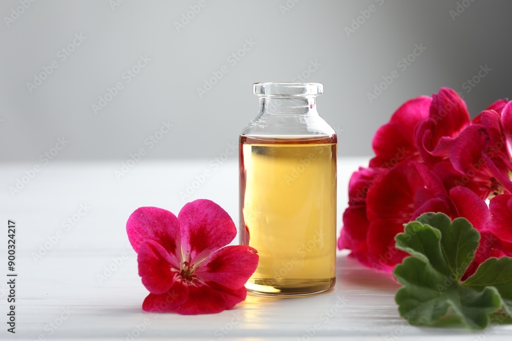Bottle of geranium essential oil and beautiful flowers on white wooden table, closeup Bottle of geranium essential oil and beautiful flowers on white wooden table, closeup