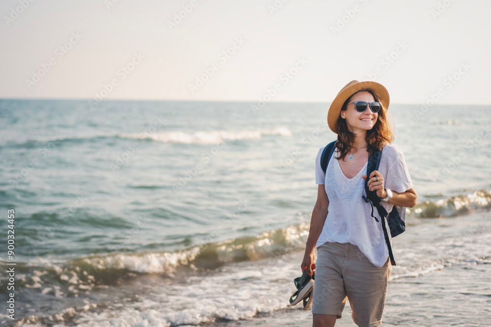 Young woman in a hat and sunglasses walking along the sea beach on a summer day
