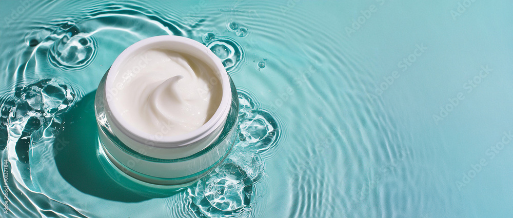 Fototapeta premium Top view of face or body cream standing in blue water with waves, drops and ripples. Presentation of cosmetic product with place for text.