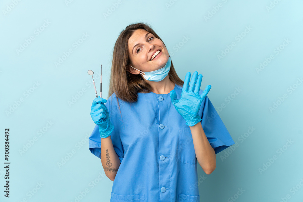 Slovak dentist holding tools isolated on blue background saluting with hand with happy expression Slovak dentist holding tools isolated on blue background saluting with hand with happy expression
