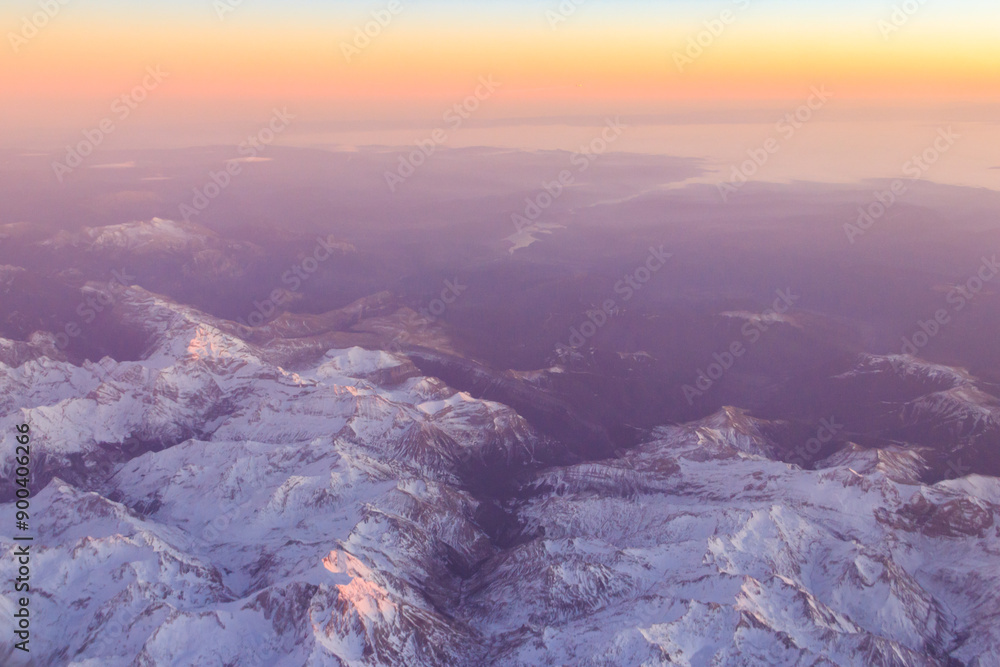 Fototapeta premium View out of an airplane window of a snow-covered mountain range at sunset
