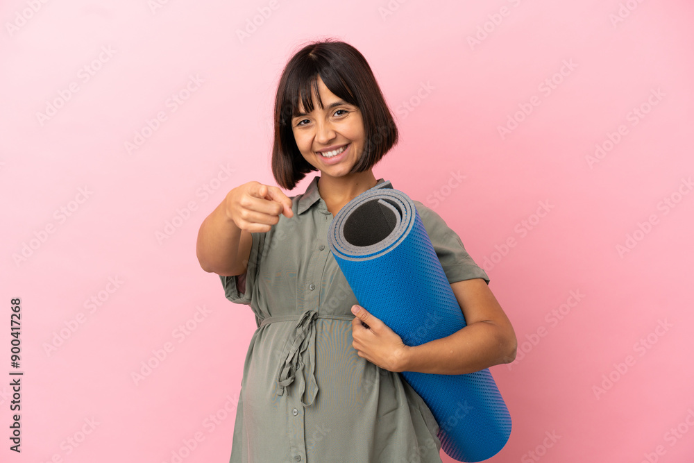 Fototapeta premium Woman over isolated background pregnant and going to yoga classes while pointing front