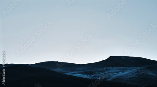 Silhouette of a dark mountain range against a pale blue sky at dusk or dawn