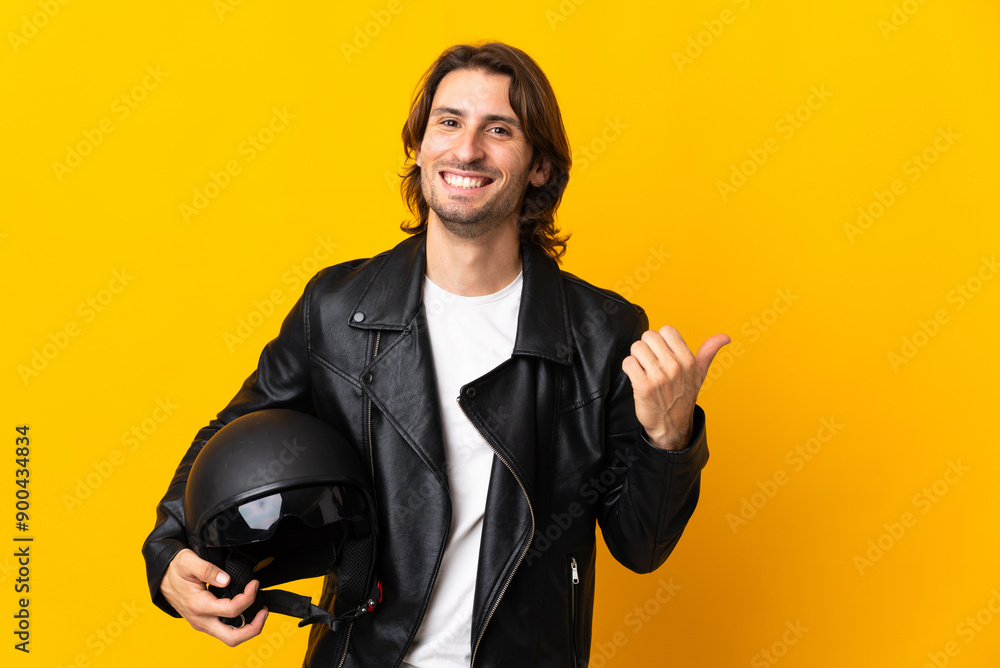 Man with a motorcycle helmet isolated on yellow background pointing to the side to present a product Man with a motorcycle helmet isolated on yellow background pointing to the side to present a product