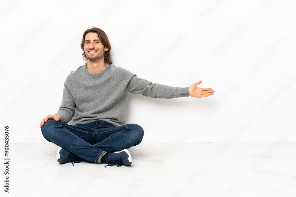 Young handsome man sitting on the floor over isolated background extending hands to the side for inviting to come Young handsome man sitting on the floor over isolated background extending hands to the side for inviting to come