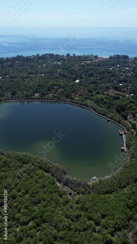 The image shows a serene, aerial view of a coastal lagoon surrounded by lush greenery with the ocean in the background, showcasing nature's beauty and tranquility. photo