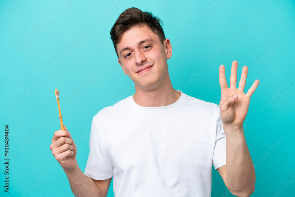 Fototapeta premium Young Brazilian man brushing teeth isolated on blue background happy and counting four with fingers