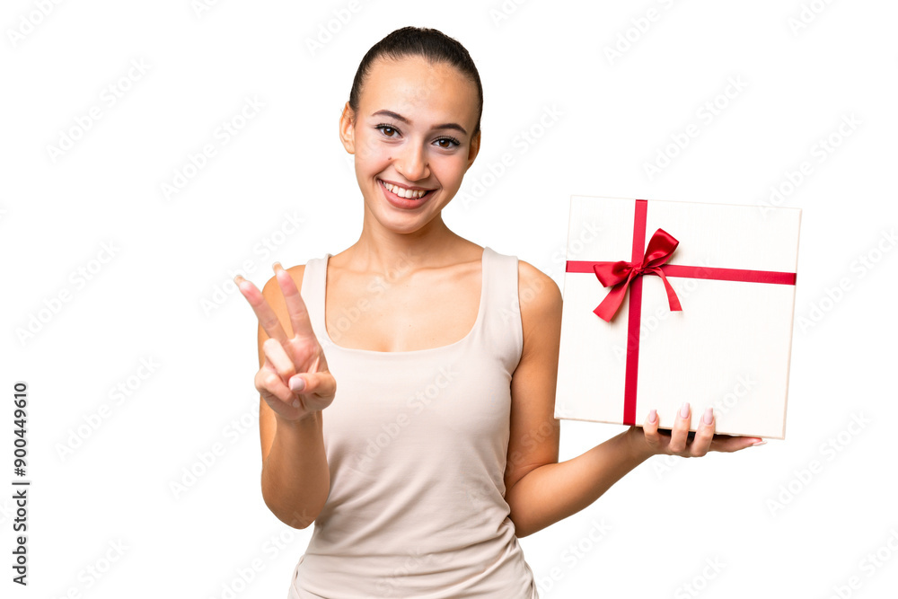 Young Arab woman holding a gift over isolated background smiling and showing victory sign Young Arab woman holding a gift over isolated background smiling and showing victory sign