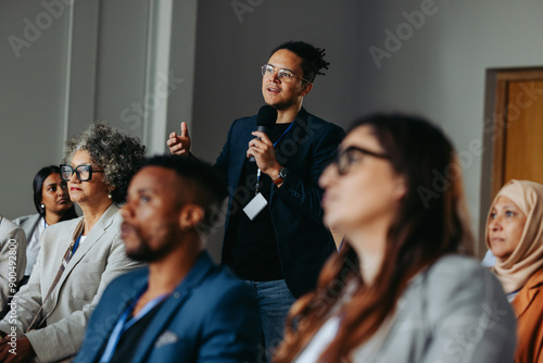 Businessman asking question during diverse conference workshop presentation