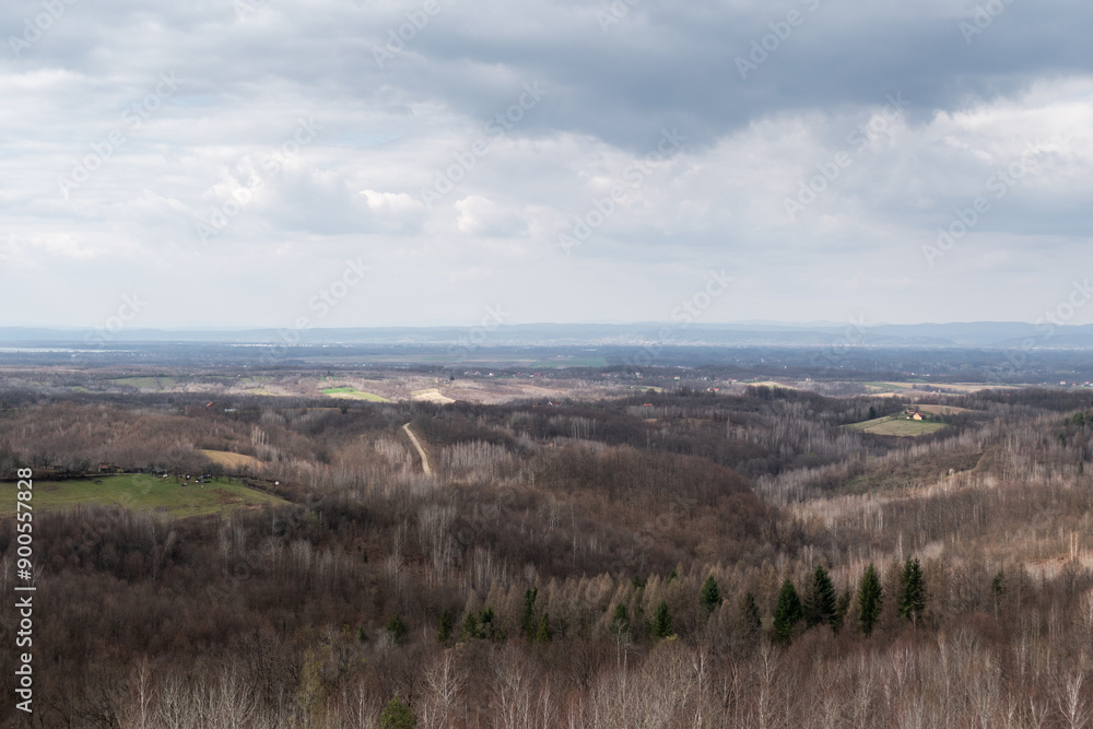 Hilly countryside during cloudy day, village with scattered houses and hills overgrown with leafless forest in March Hilly countryside during cloudy day, village with scattered houses and hills overgrown with leafless forest in March
