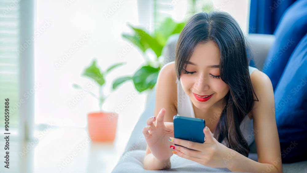 Young Asian woman using mobile phone to talk with friend on sofa at living room at home.
Young Asian woman using mobile phone to talk with friend on sofa at living room at home.