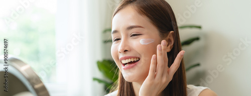 Free Download Facial beauty skin health care, smile of cute asian young woman looking at mirror, hand applying moisturizer lotion on her face, female putting cream treatment before makeup cosmetic routine at home. - GFXLoad