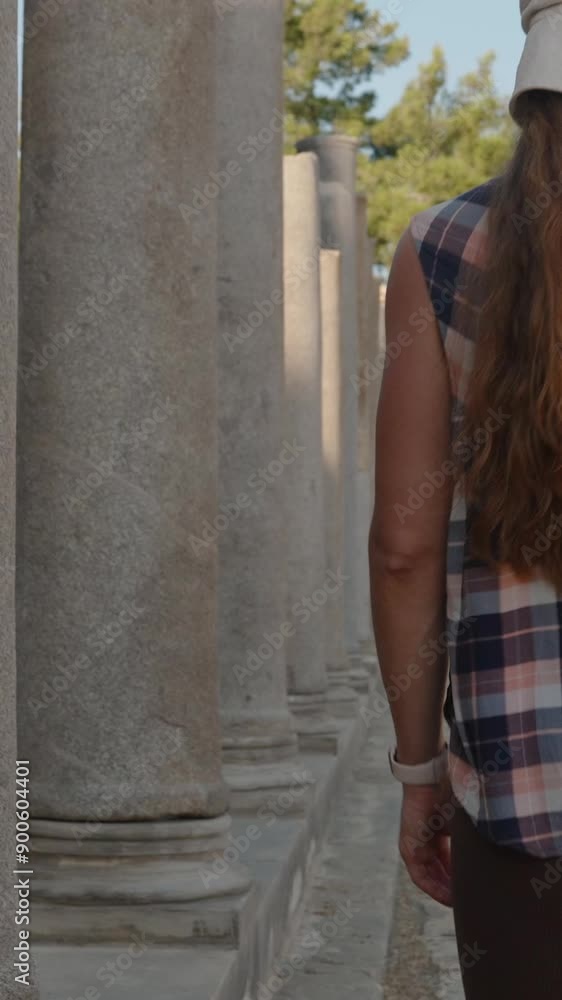 Vertical video. A Woman Walks Along the Path of an Ancient Ruin, Flanked by Majestic Stone Columns and Sunlit Shadows. Vertical video. A Woman Walks Along the Path of an Ancient Ruin, Flanked by Majestic Stone Columns and Sunlit Shadows.