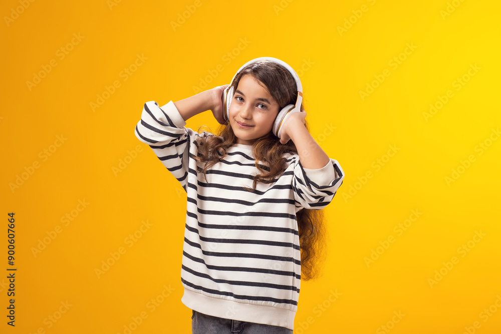 Smiling kid girl enjoying music in headphones on yellow background. Lifestyle and leasure concept Smiling kid girl enjoying music in headphones on yellow background. Lifestyle and leasure concept