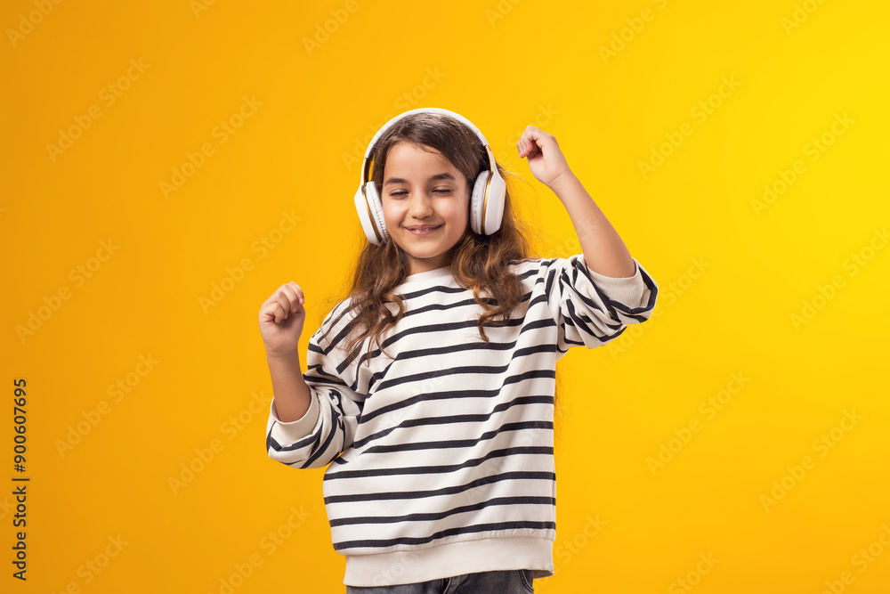 Smiling kid girl enjoying music in headphones on yellow background. Lifestyle and leasure concept Smiling kid girl enjoying music in headphones on yellow background. Lifestyle and leasure concept
