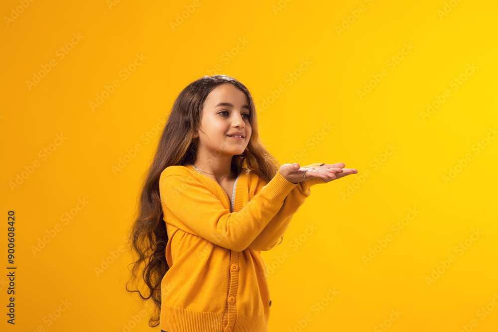 Smiling preteen girl pointing with palms to an empty place on yellow background. Advertisement concept Smiling preteen girl pointing with palms to an empty place on yellow background. Advertisement concept
