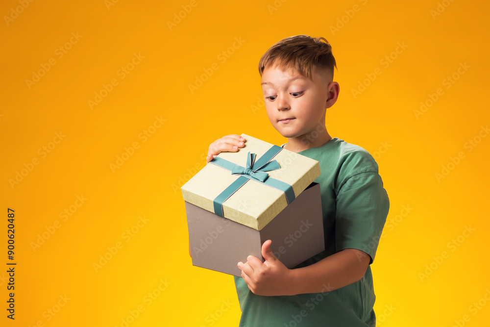 Child boy holding giftbox and looking inside the box over yellow background. Birthday and celebration concept Child boy holding giftbox and looking inside the box over yellow background. Birthday and celebration concept