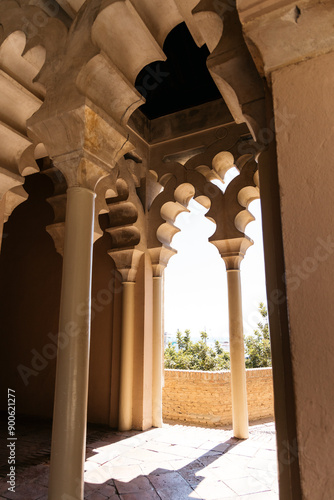 interior with arched columns typical of Moorish architecture. Light enters through the arched openings, creating a contrast of shadows and illuminated areas. The columns and arches have a complex, dec