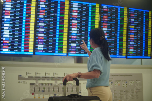 A female tourist carefully examines the detailed travel schedule for her upcoming flight at the busy airport. photo