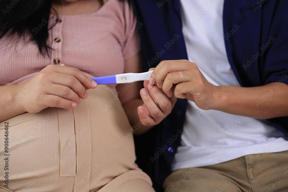 Happy man with pregnant wife rubbing his belly while relaxing and spending time in modern apartment. Pregnant woman and husband spending time together using smartphone Happy man with pregnant wife rubbing his belly while relaxing and spending time in modern apartment. Pregnant woman and husband spending time together using smartphone